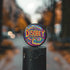 Round black pinback button with neon embroidery-style waves surrounding bold yellow and red "DISOBEY" text.